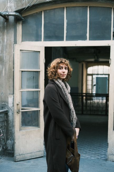 A woman stands in an old doorway with vintage architecture, wearing a scarf.