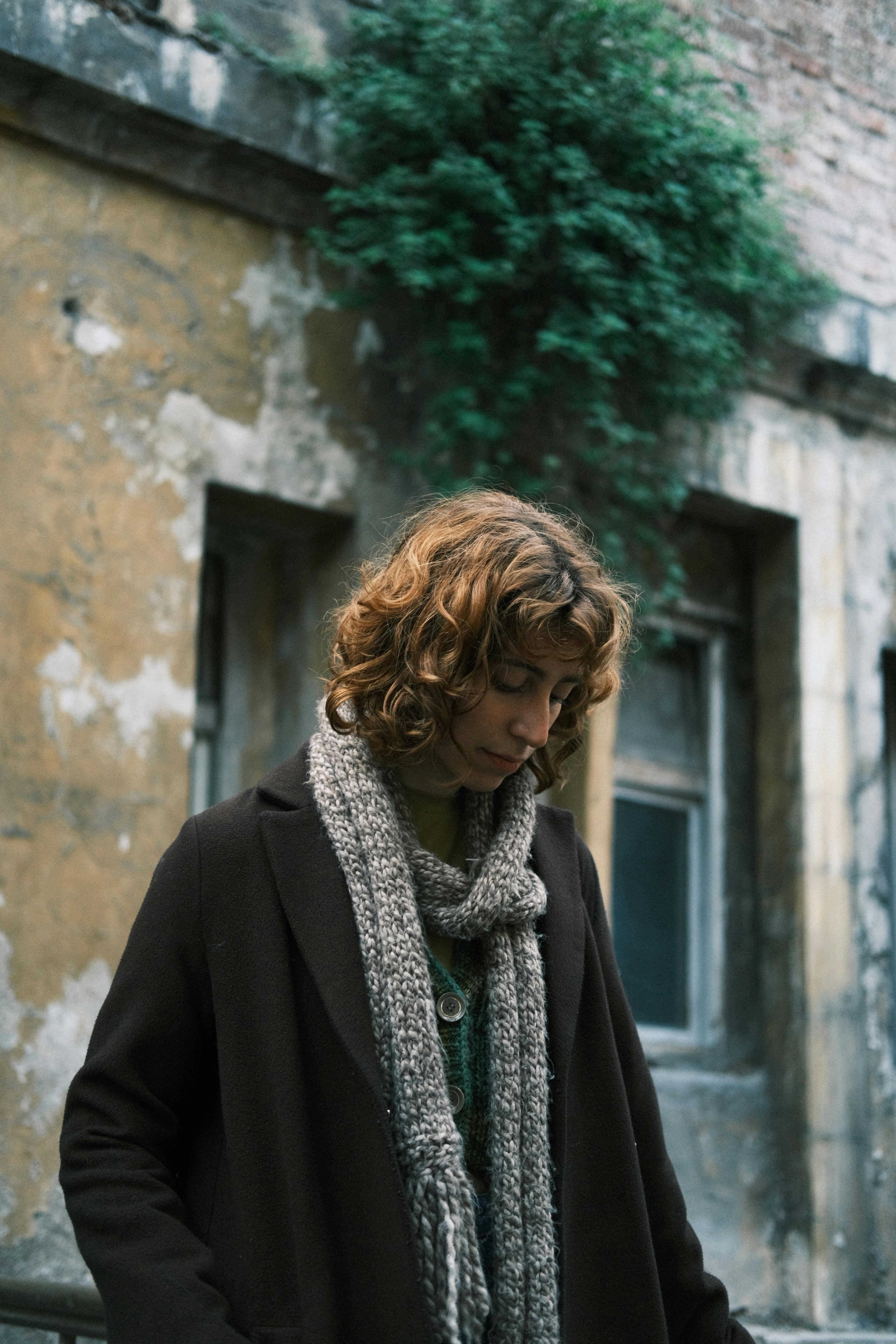 Thoughtful woman in warm clothing against an urban, textured backdrop.