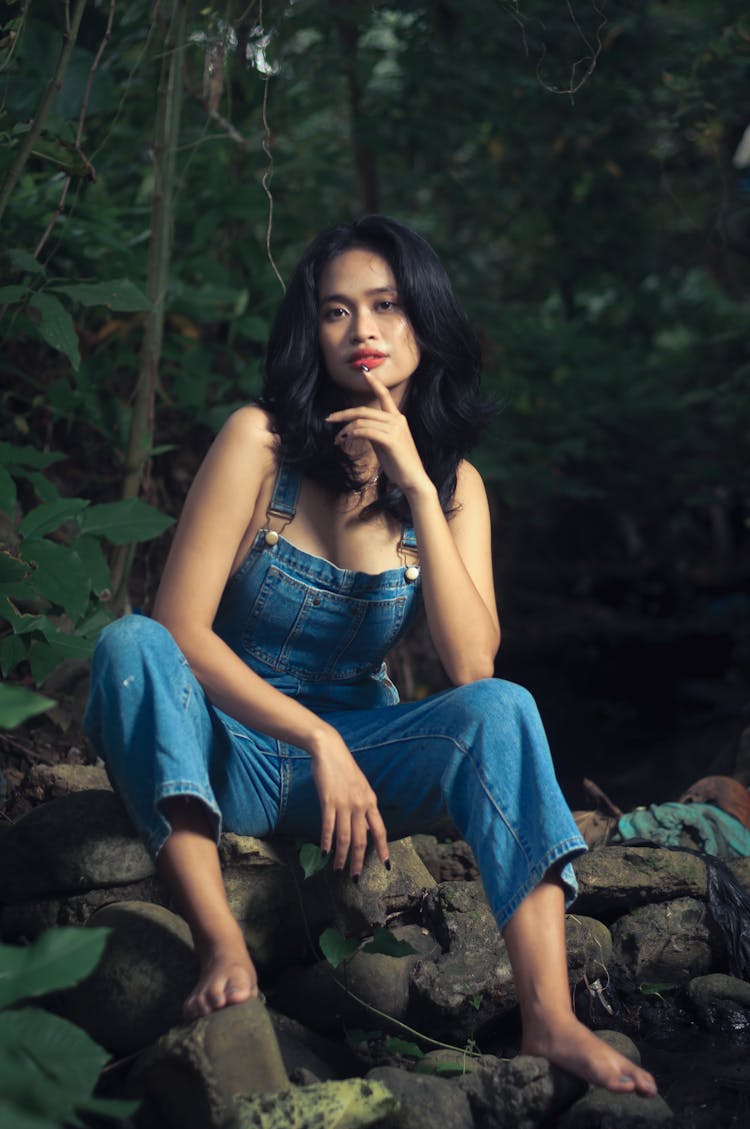 Woman In Jean Overalls Sitting In Forest