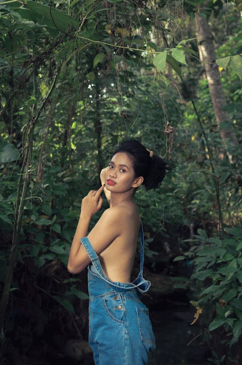 Young Woman in Denim Overalls Posing in a Forest