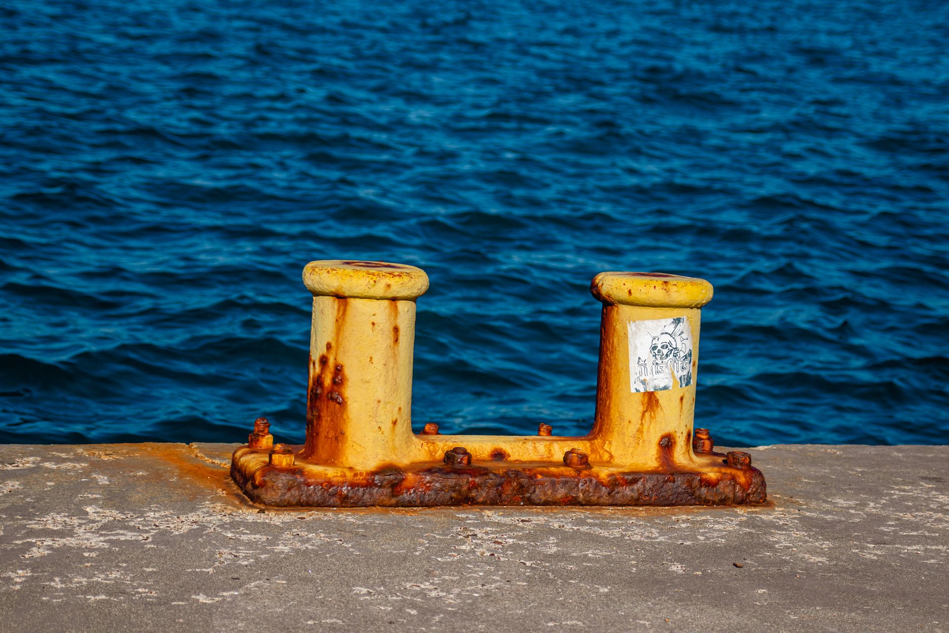 Rusty bollards on a concrete dock beside the blue ocean, showcasing rustic charm.