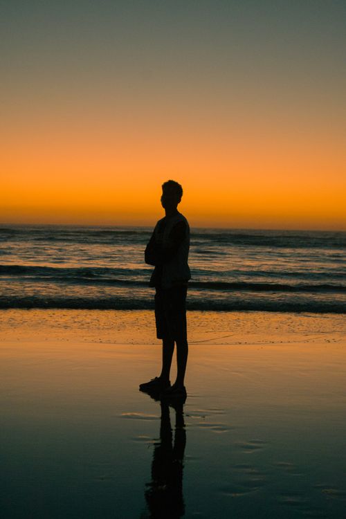 Free A silhouette of a man standing on the beach during a vibrant Moroccan sunset. Stock Photo