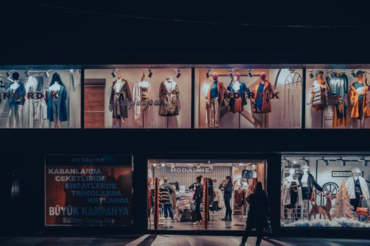 Illuminated fashion store window with mannequins and dramatic lighting at night.