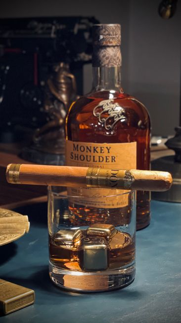 Elegant still life of Monkey Shoulder whiskey bottle with cigar and glass of scotch.