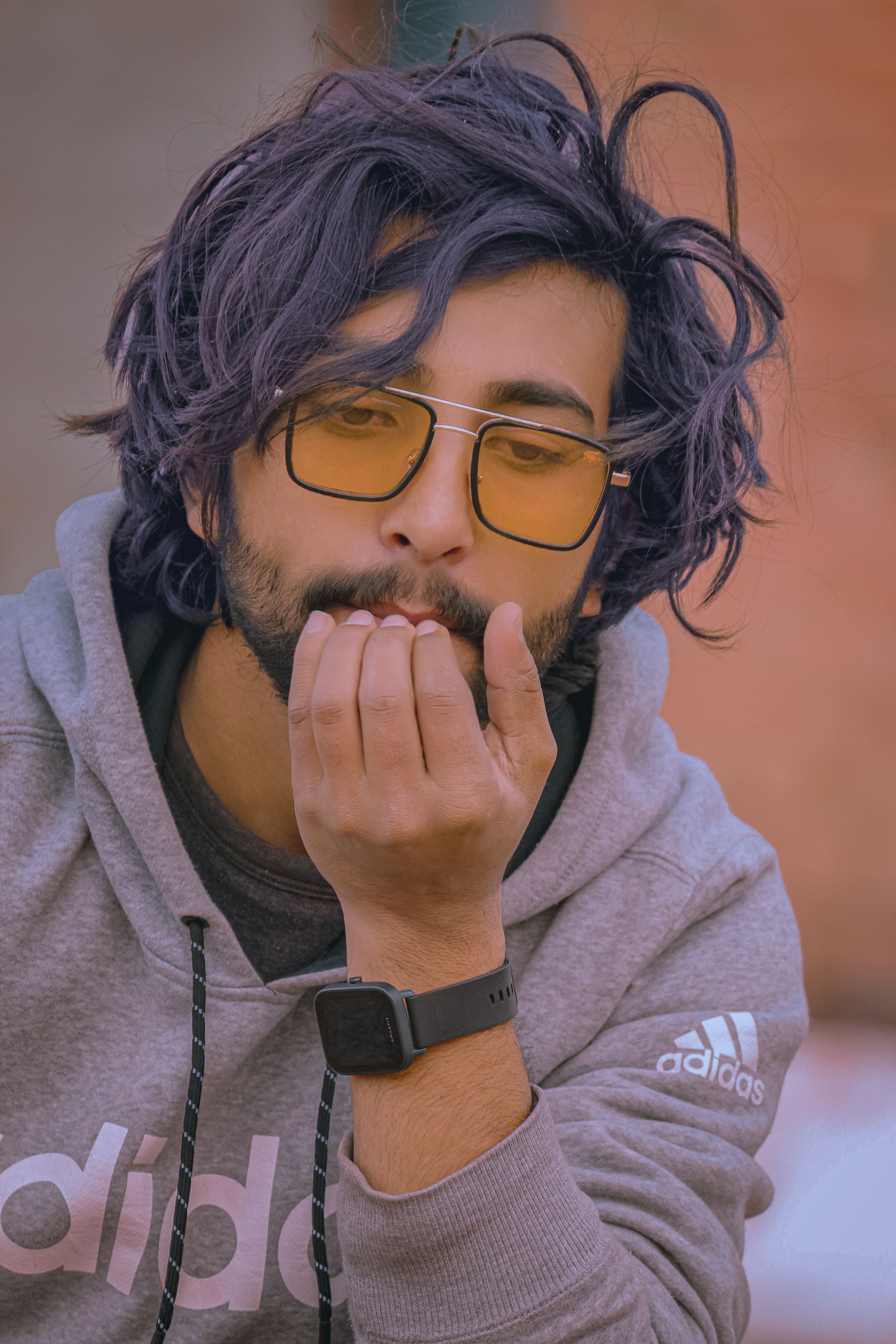 A modern man in a gray hoodie and sunglasses with messy hair and a smartwatch.