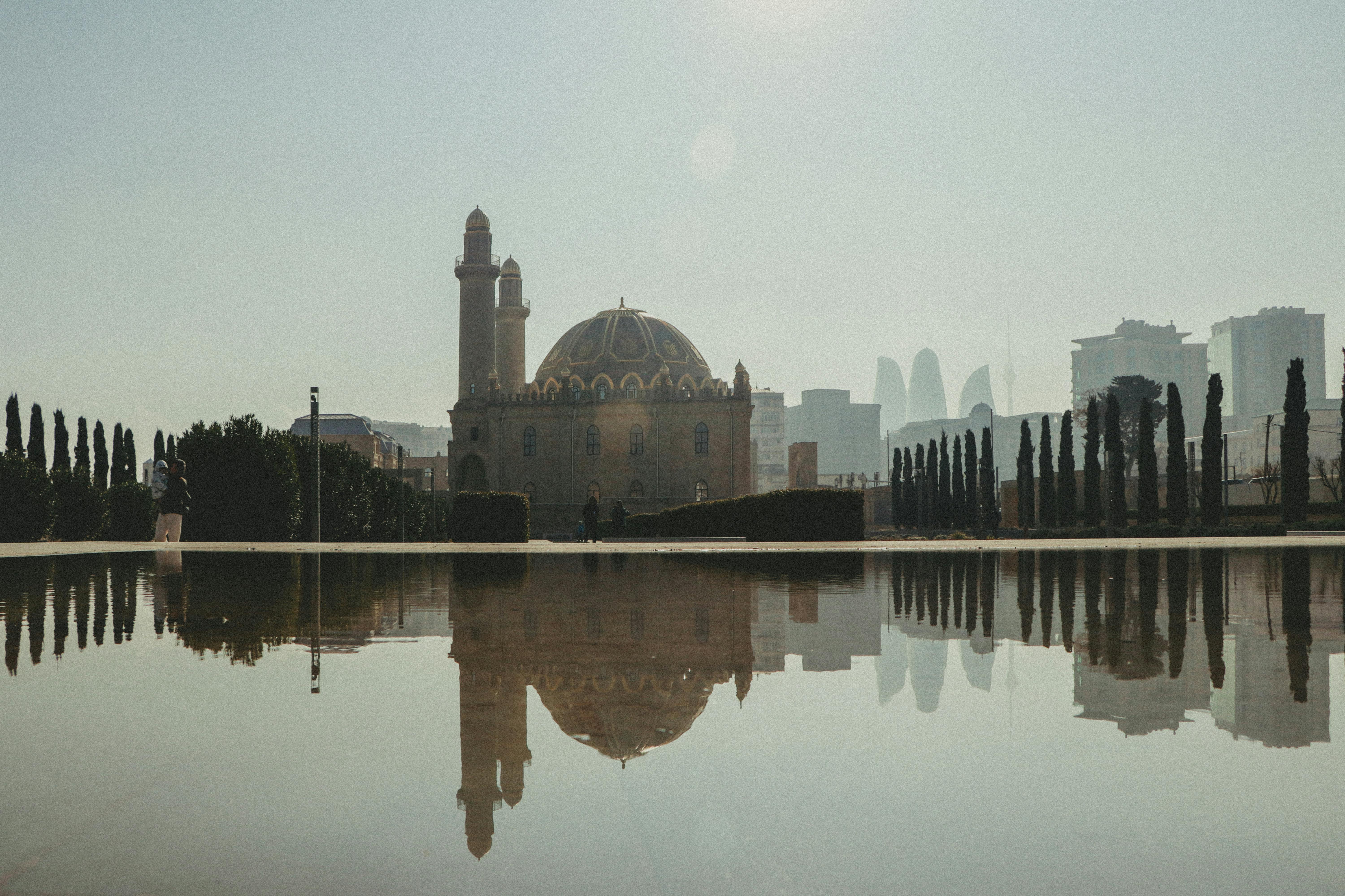Elegant mosque reflection in a city reservoir with urban skyline backdrop.