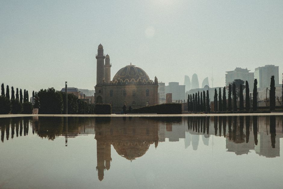 Elegant mosque reflection in a city reservoir with urban skyline backdrop.