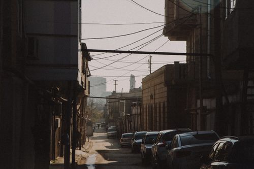 Free A quiet city street with parked cars and buildings under a clear sky, creating an urban ambiance. Stock Photo