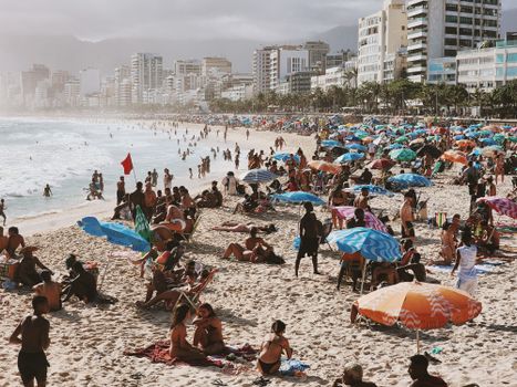 Crowded beach scene with umbrellas and beachgoers enjoying a sunny summer day.