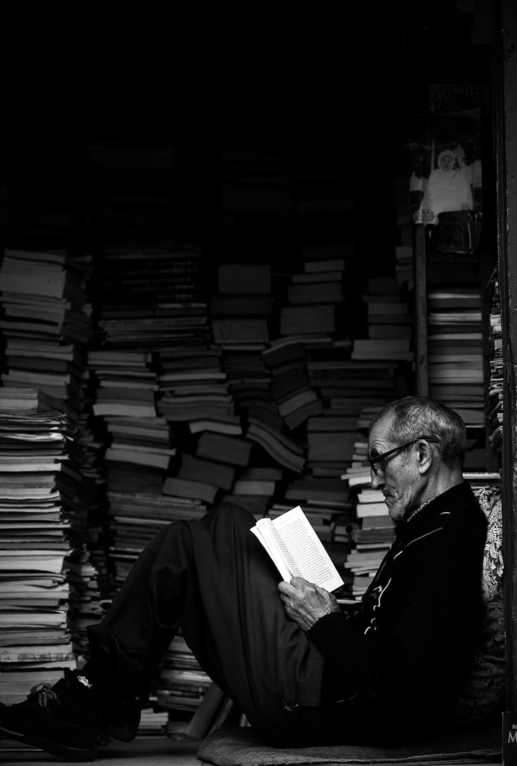 Man Reading Book By Stack Of Books