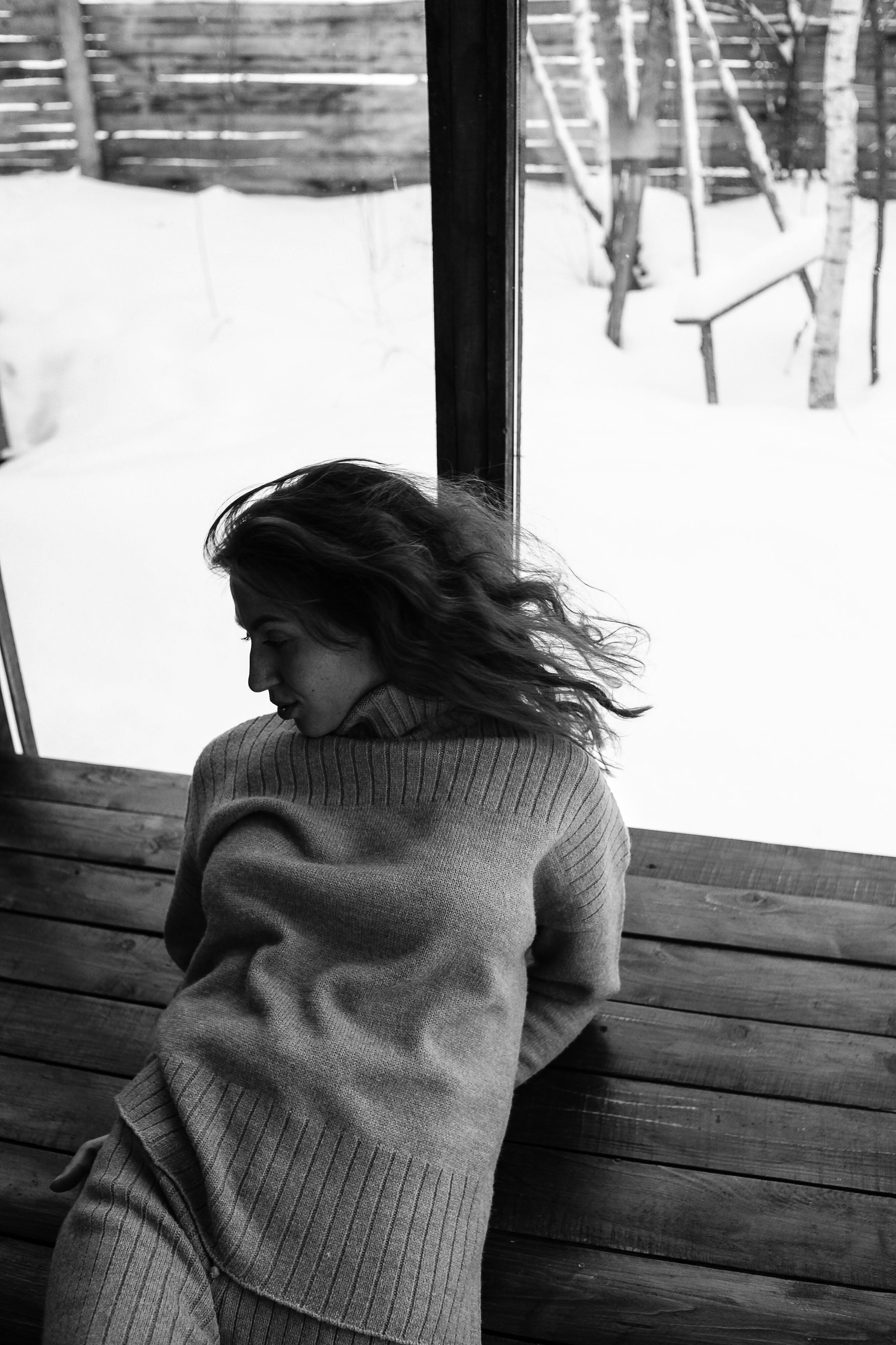 Elegant black and white portrait of a woman sitting indoors with a snowy background.