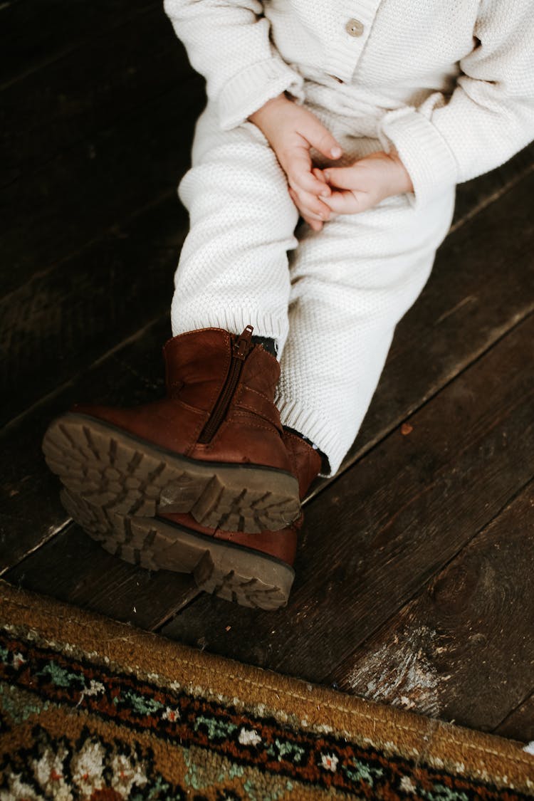 Child In Winter Boots Sitting On Wooden Floor