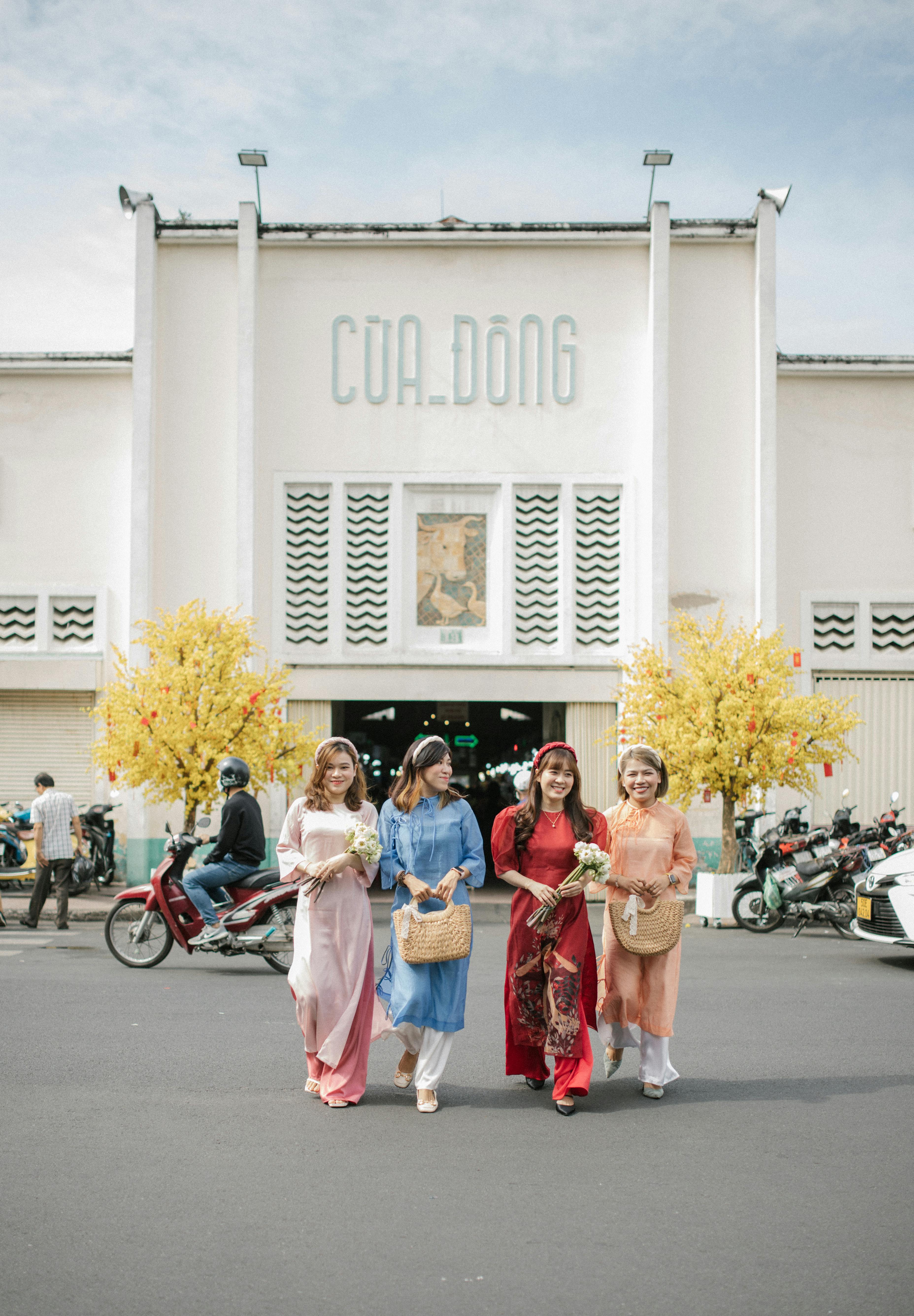 Four women in traditional attire smiling outside Cua Dong market, vibrant and joyful scene.