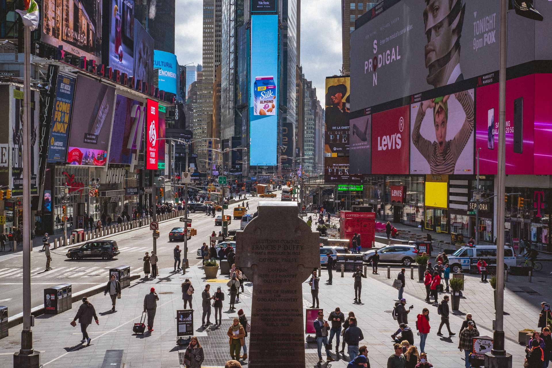 Bright daytime view of Times Square NYC with colorful digital billboards, tall buildings, and crowds of pedestrians