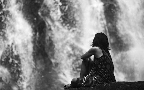 A woman sitting on a rock looking at a waterfall