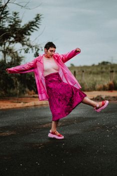 Woman in pink outfit dances on a rural road in Mirassol, showcasing vibrant fashion.