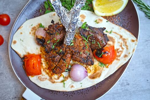 Delicious grilled meat skewers served on flatbread with roasted vegetables and lemon.