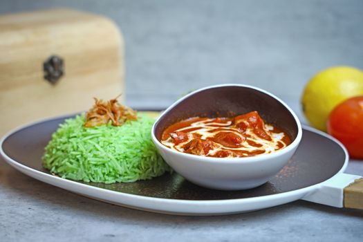Appetizing platter of chicken curry served with vibrant green rice and garnished with vegetables.