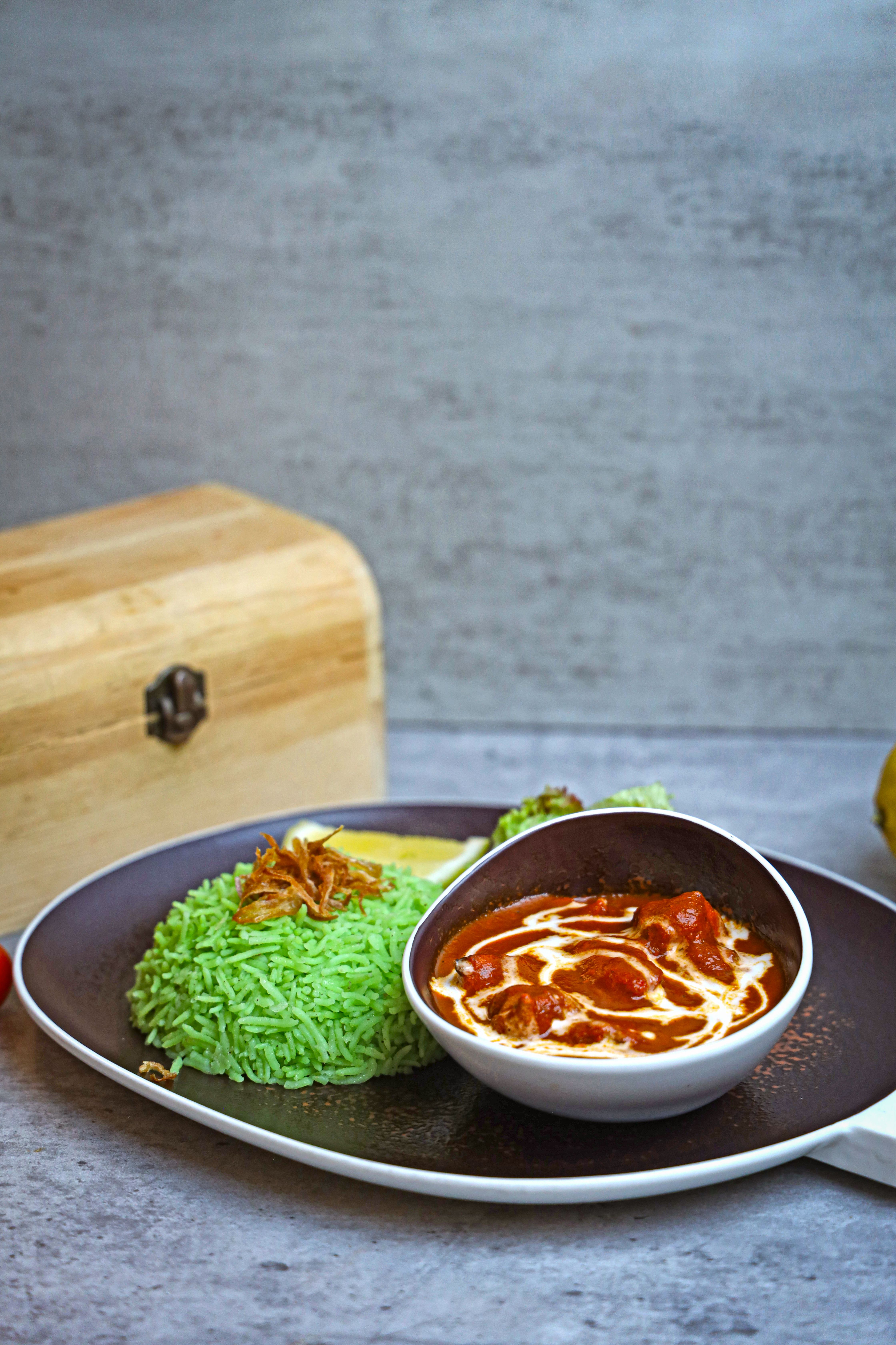 A flavorful green rice dish served with a spicy curry and garnishes, ideal for food photography.