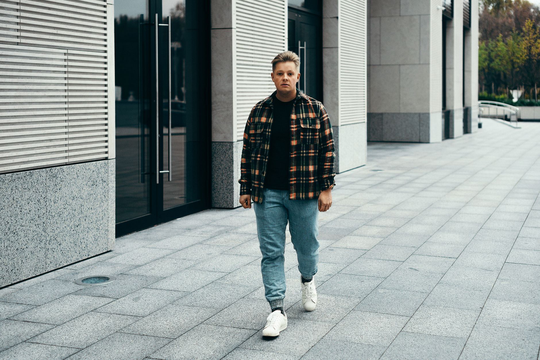 Young man walking on a stone pavement in Minsk, wearing a plaid shirt and jeans.
