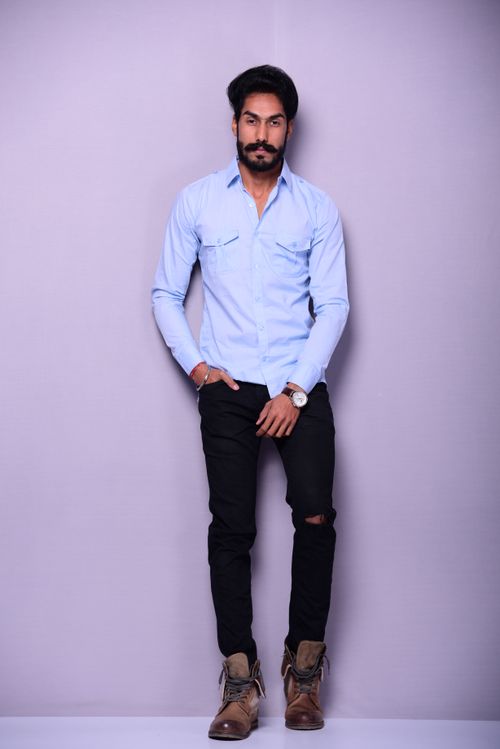 Free Stylish man modeling in a blue shirt and jeans against a neutral backdrop. Stock Photo
