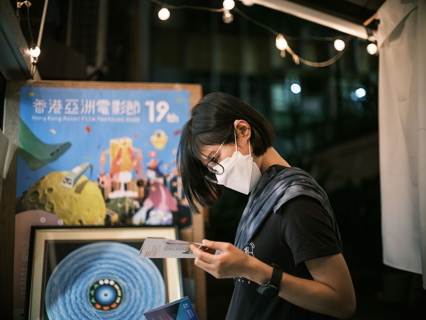 Side view of a woman wearing a face mask, reading a brochure by a film festival poster.