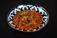 Close-up of a spicy Asian dish served on an ornate plate against a black background.