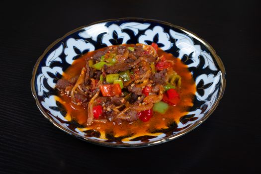Close-up of a spicy Asian dish served on an ornate plate against a black background.