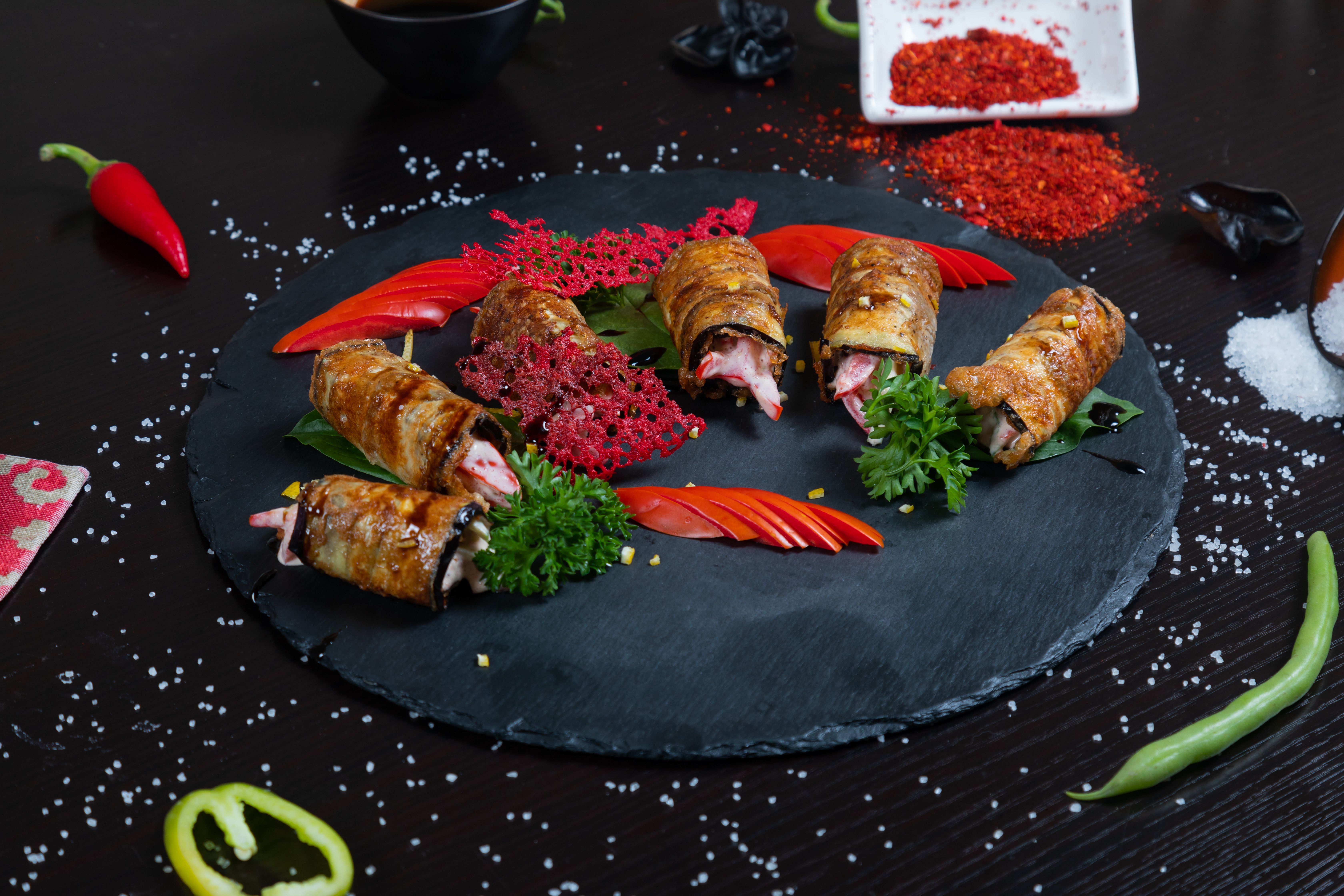 Delicious eggplant rolls with vibrant garnish and spices on a black slate platter. Perfect for food lovers.