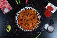Delicious spicy Asian dish with red sauce, garnished with peppers and spices, captured on a black background.