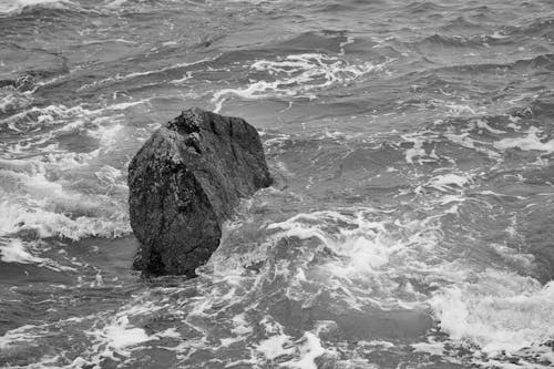 Grayscale Photo of Waves Crashing on Black Granite Boulder