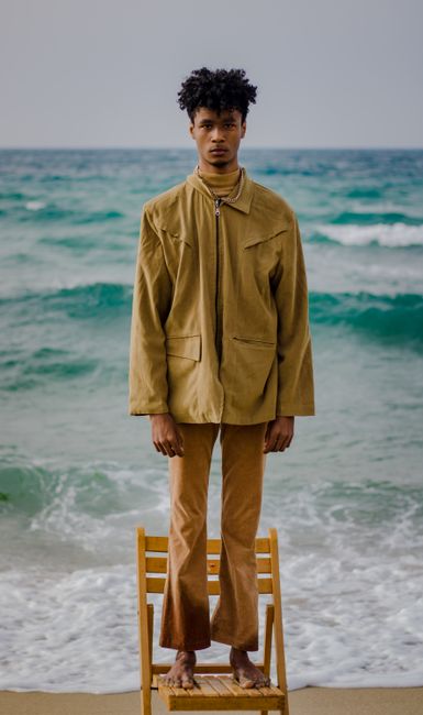 Fashionable man on chair by the sea with a contemplative pose.