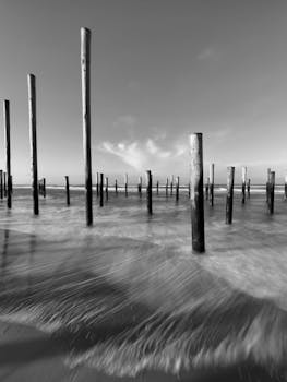 Black and white long exposure shot of ocean poles with waves at a beach shore.