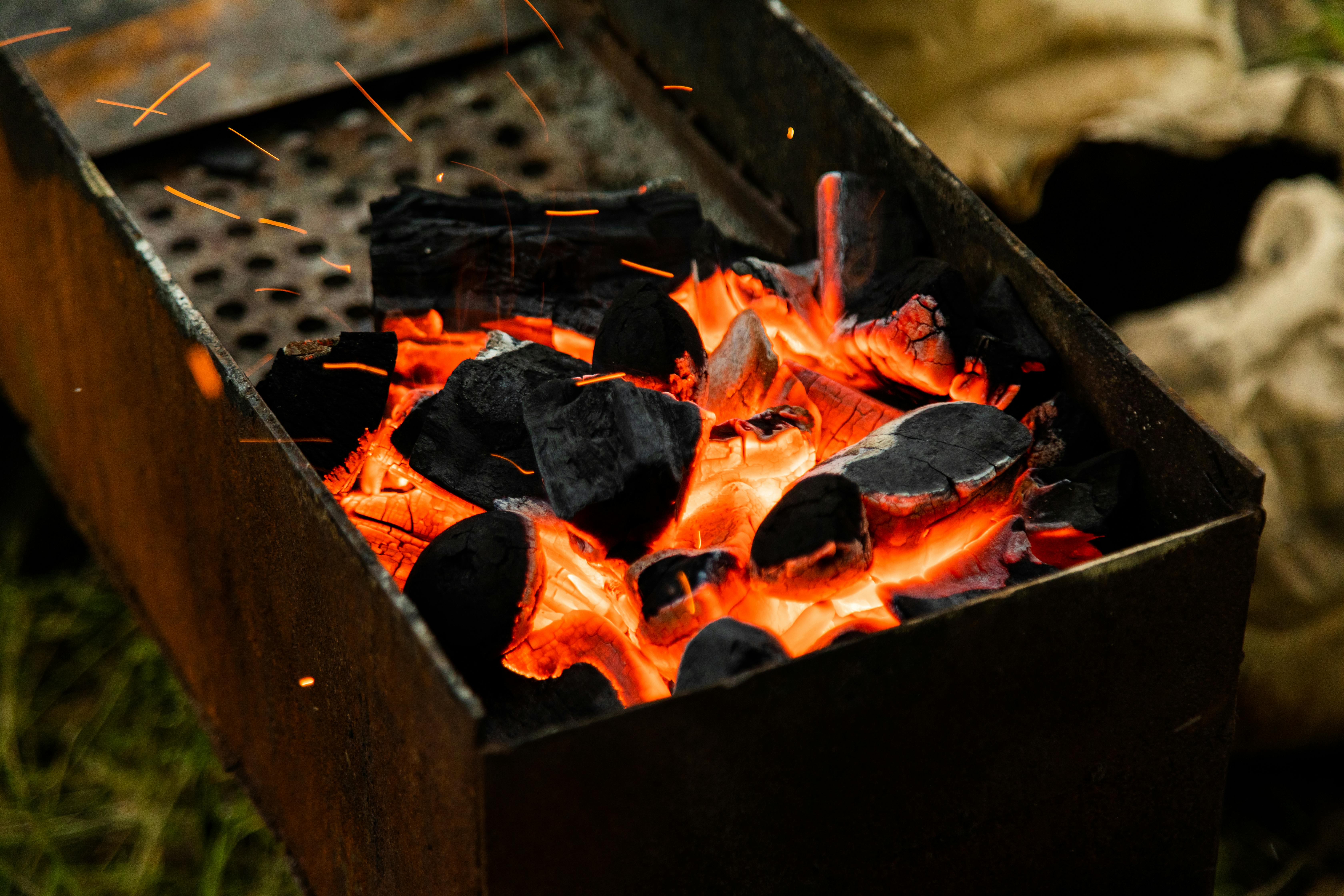 Glowing charcoal emits heat and sparks in a barbecue grill. Ideal for outdoor cooking.