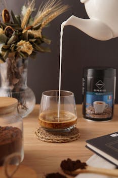 Warm and inviting image of milk being poured into espresso on a wooden table with decor.