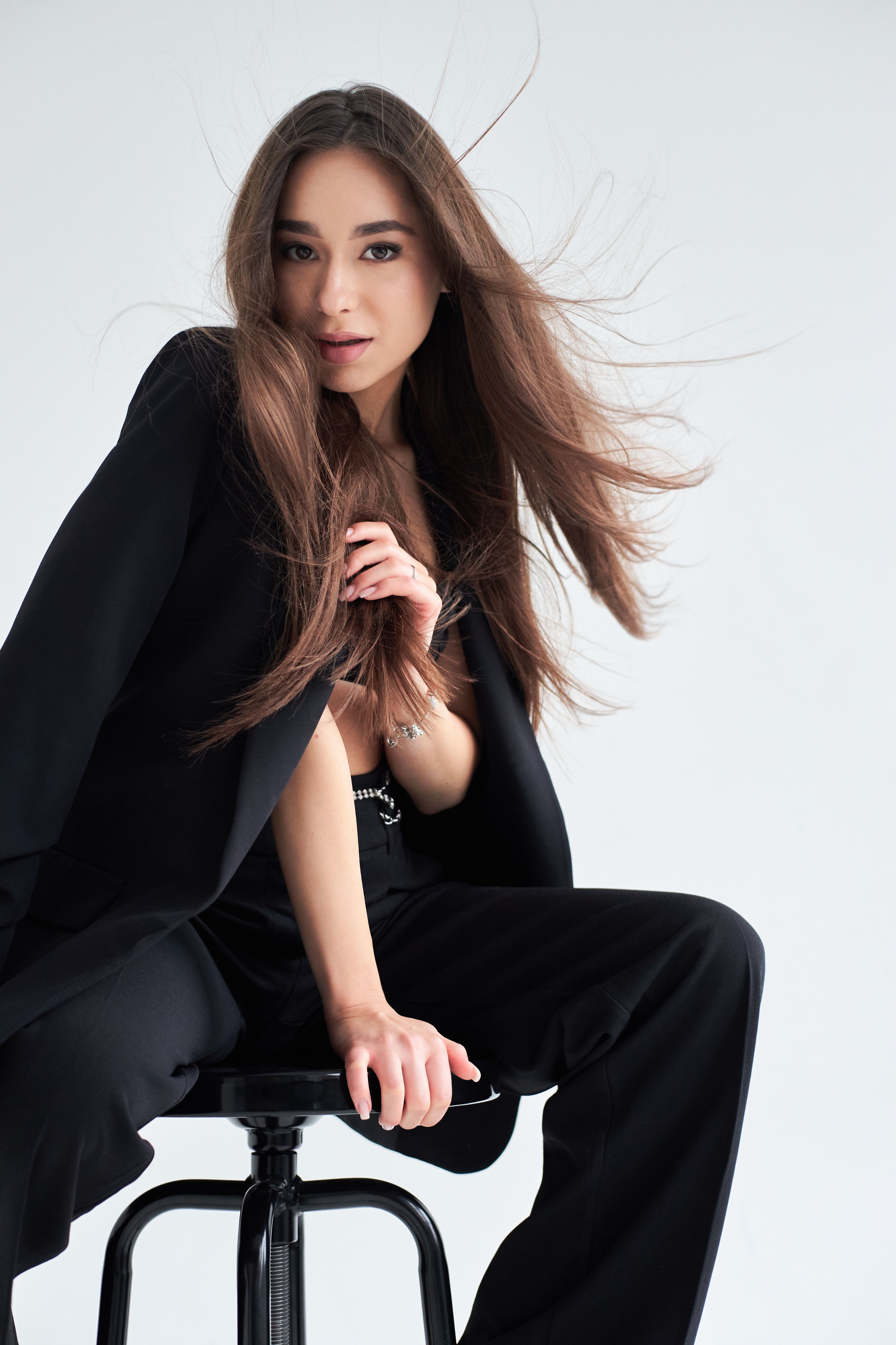Stylish brunette woman posing elegantly on a stool in a modern studio setting.