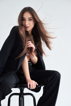 Stylish brunette woman posing elegantly on a stool in a modern studio setting.