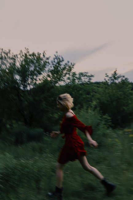 A vibrant blur of a woman in a red dress running through a lush green outdoor setting.