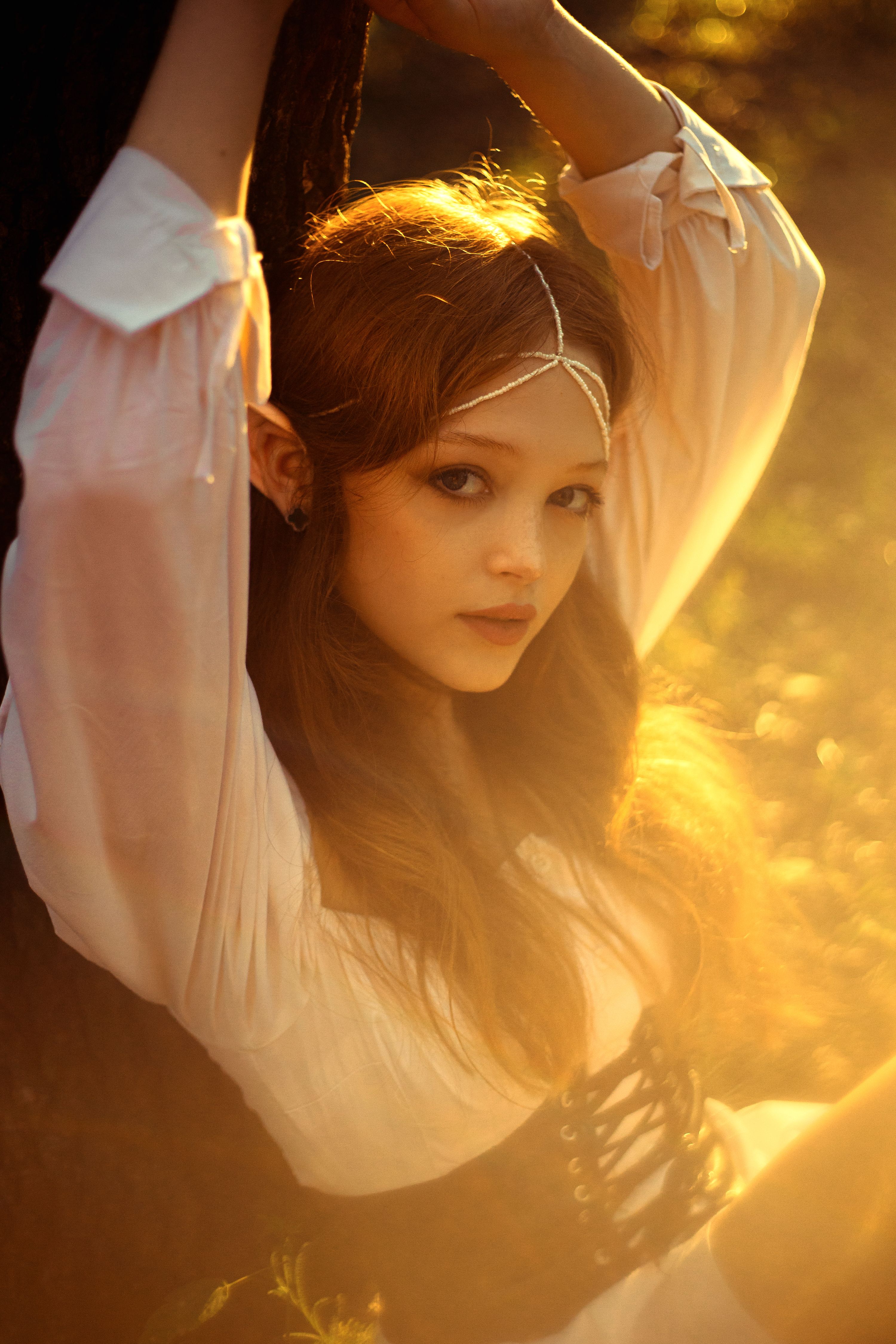 Beautiful woman in elegant attire basking in warm, dreamy sunlight outdoors.