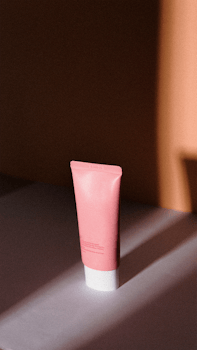 Stylish pink skincare tube in a dramatic shadow-filled indoor setting, perfect for beauty promotions.