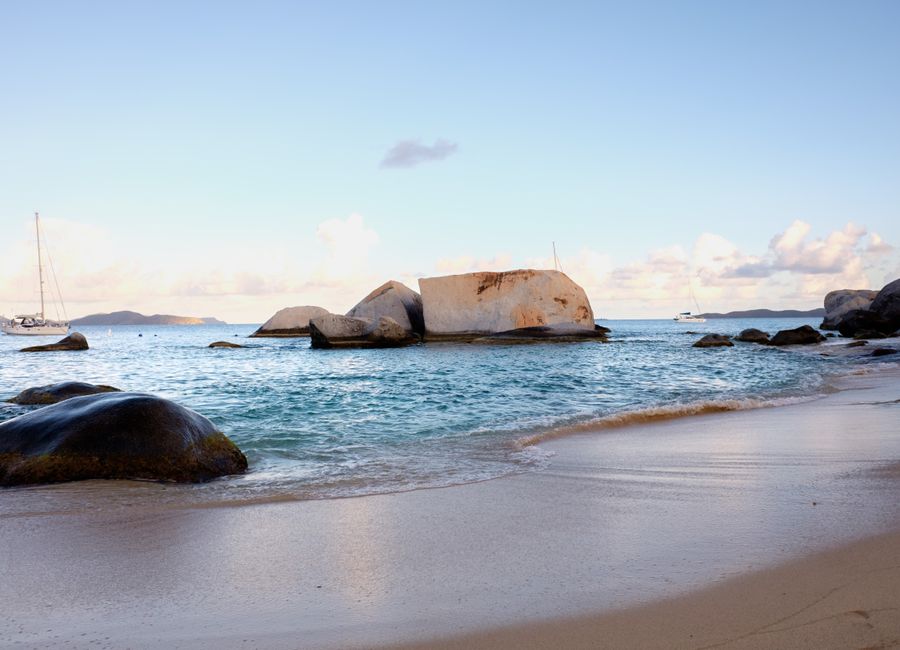 Serene coastal view with rocks, sandy beach, and boats at sunset.