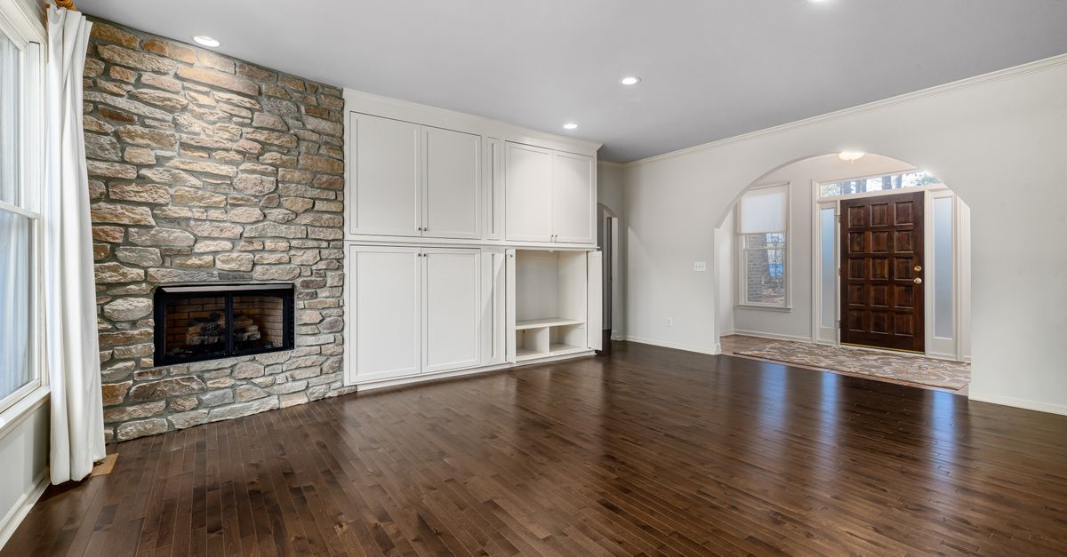 Spacious modern living room with stone fireplace, wooden flooring, and natural light.