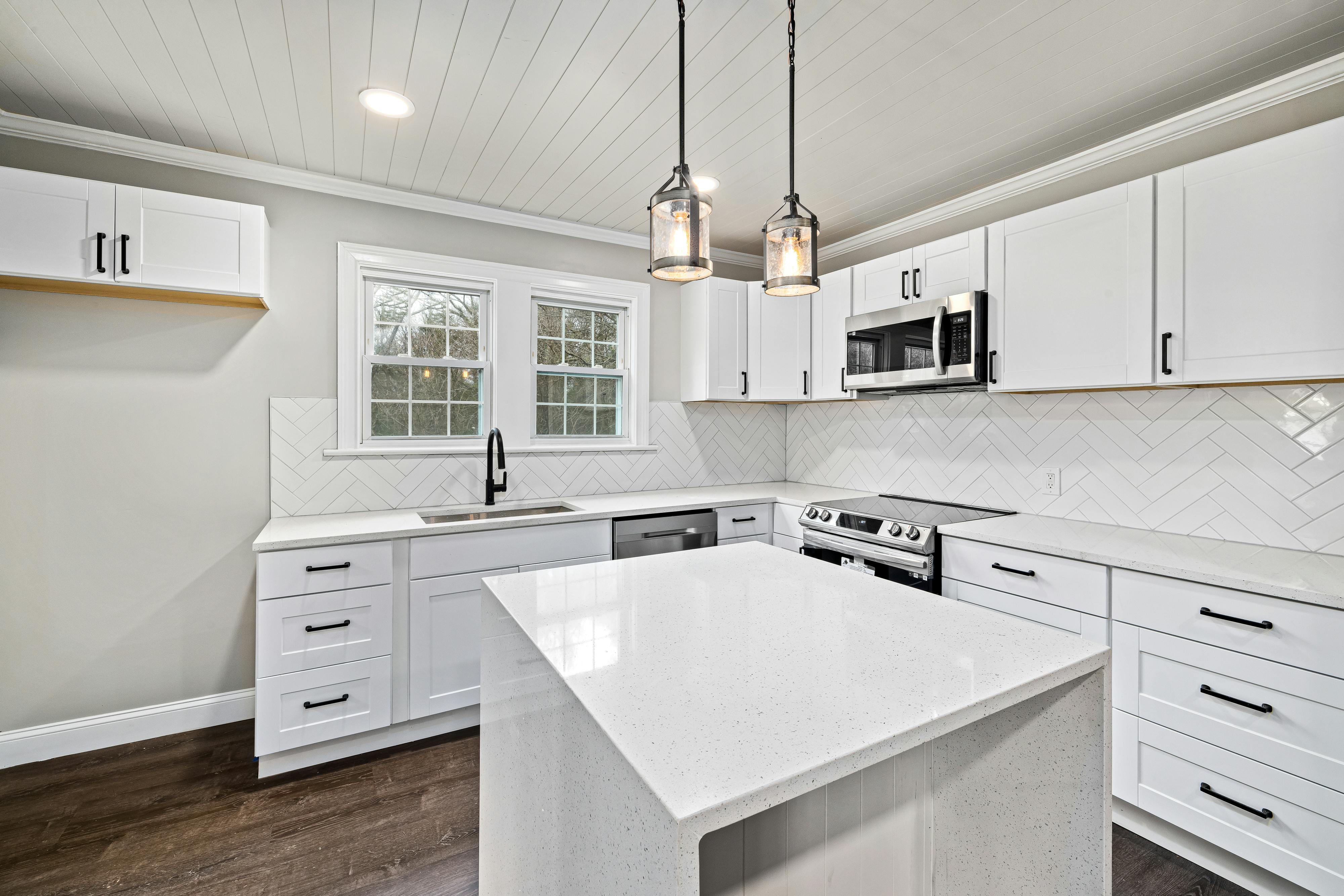 Bright modern kitchen interior with white cabinetry, island, and pendant lights.