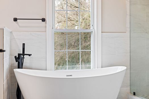 A stylish modern bathroom featuring a freestanding bathtub and large window, ideal for relaxation.