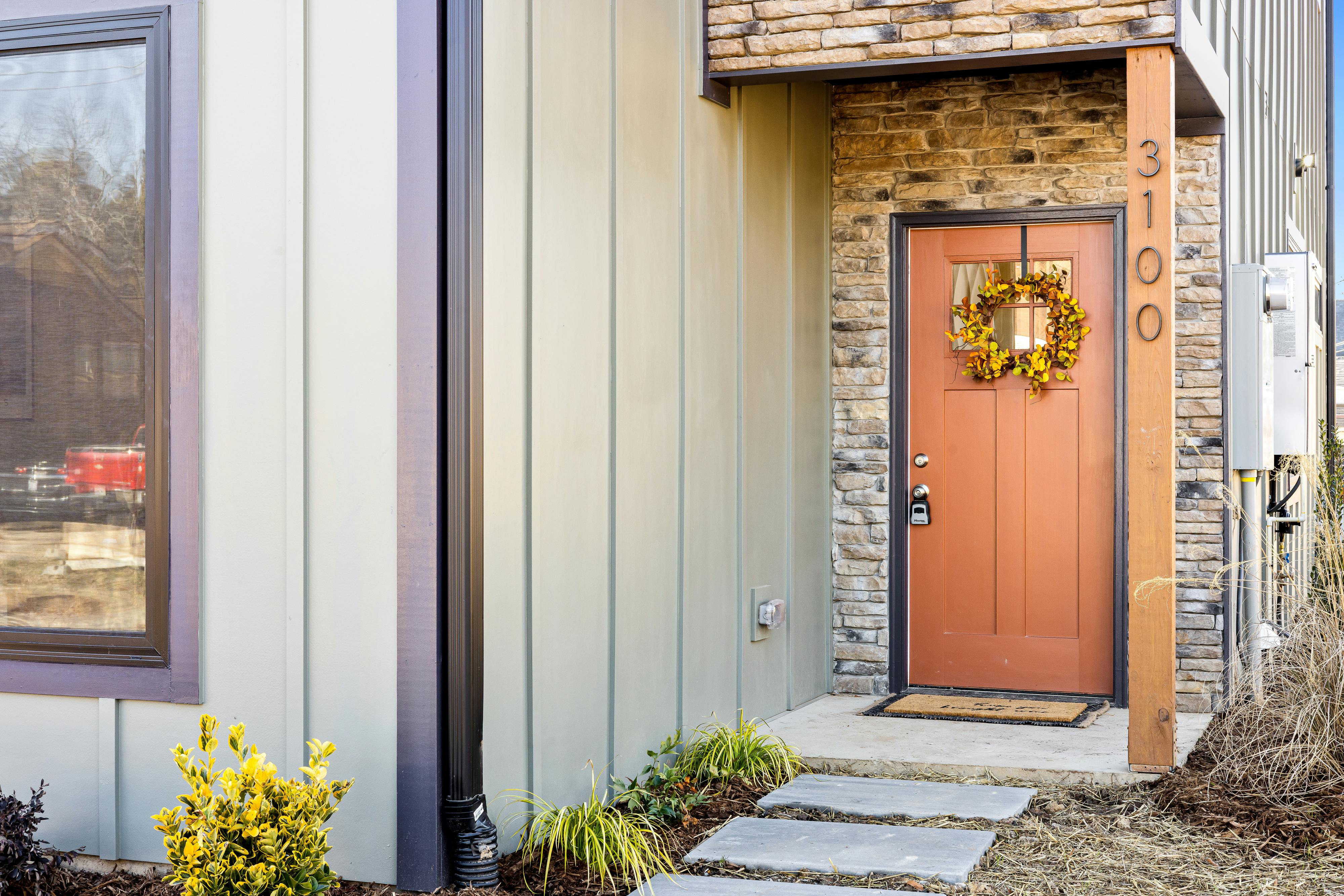 Modern house entrance with an autumn wreath on a red door, surrounded by stone and wood accents.