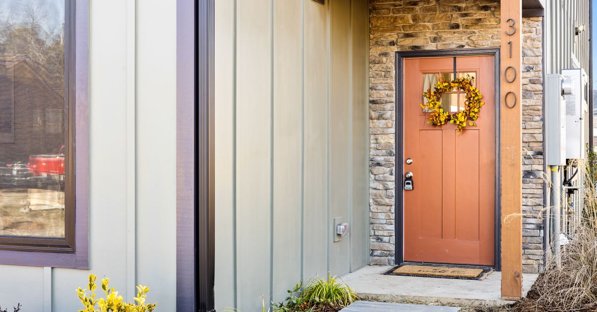 Modern house entrance with an autumn wreath on a red door, surrounded by stone and wood accents.