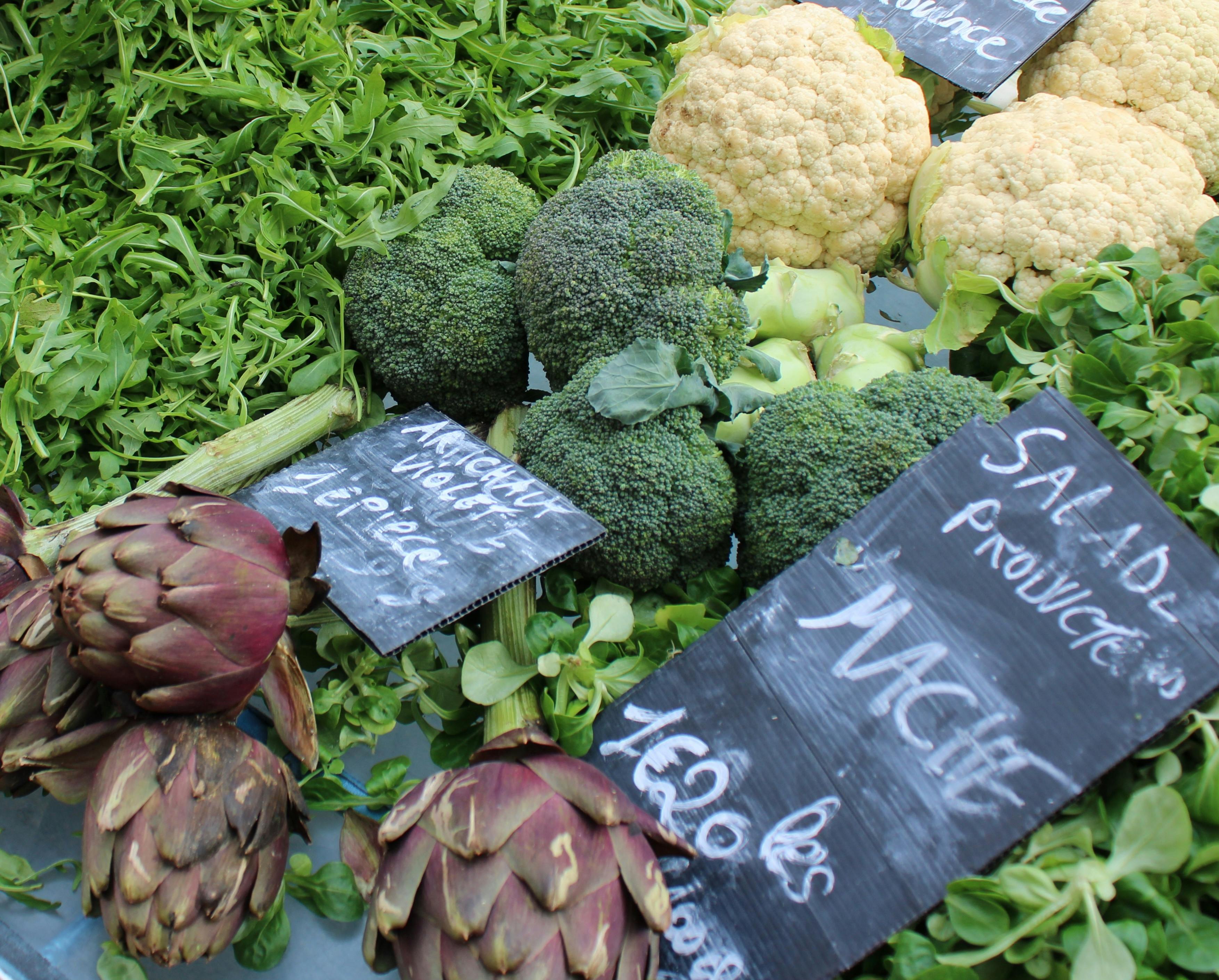 A vibrant selection of fresh vegetables including broccoli, artichokes, and greens at a local market stall.