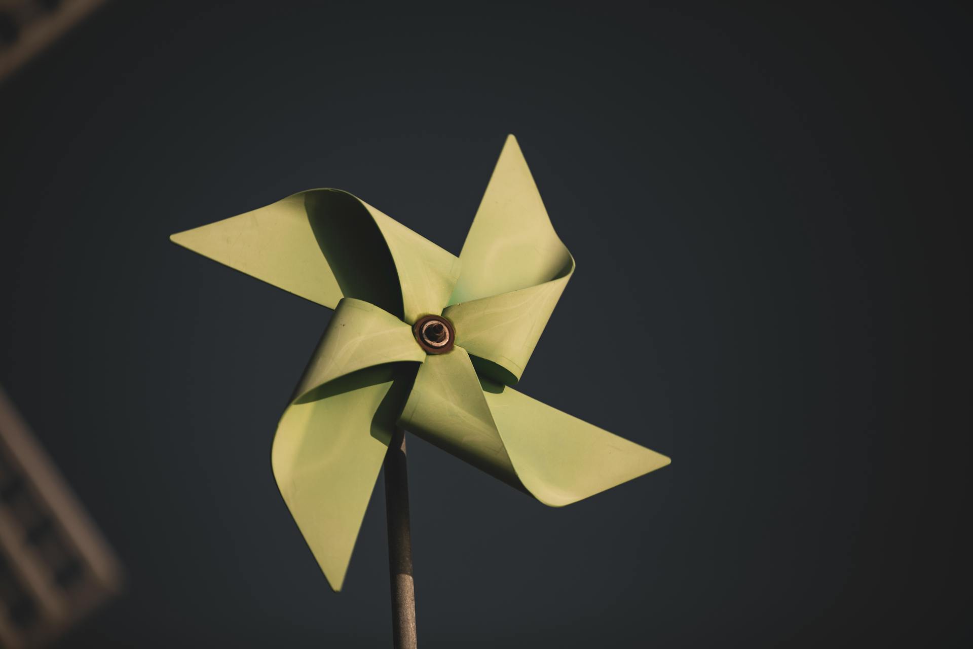 Green paper origami pinwheel against a dark background, highlighting minimalist design.