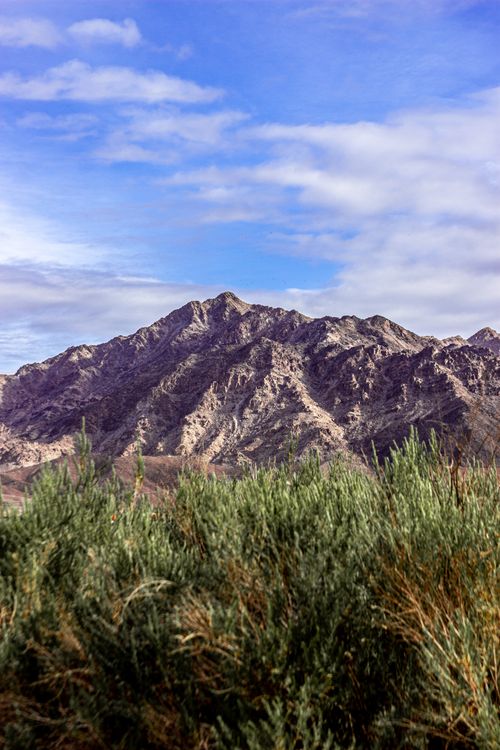 Free Stunning view of a rocky mountain with green bushes under a blue sky. Stock Photo