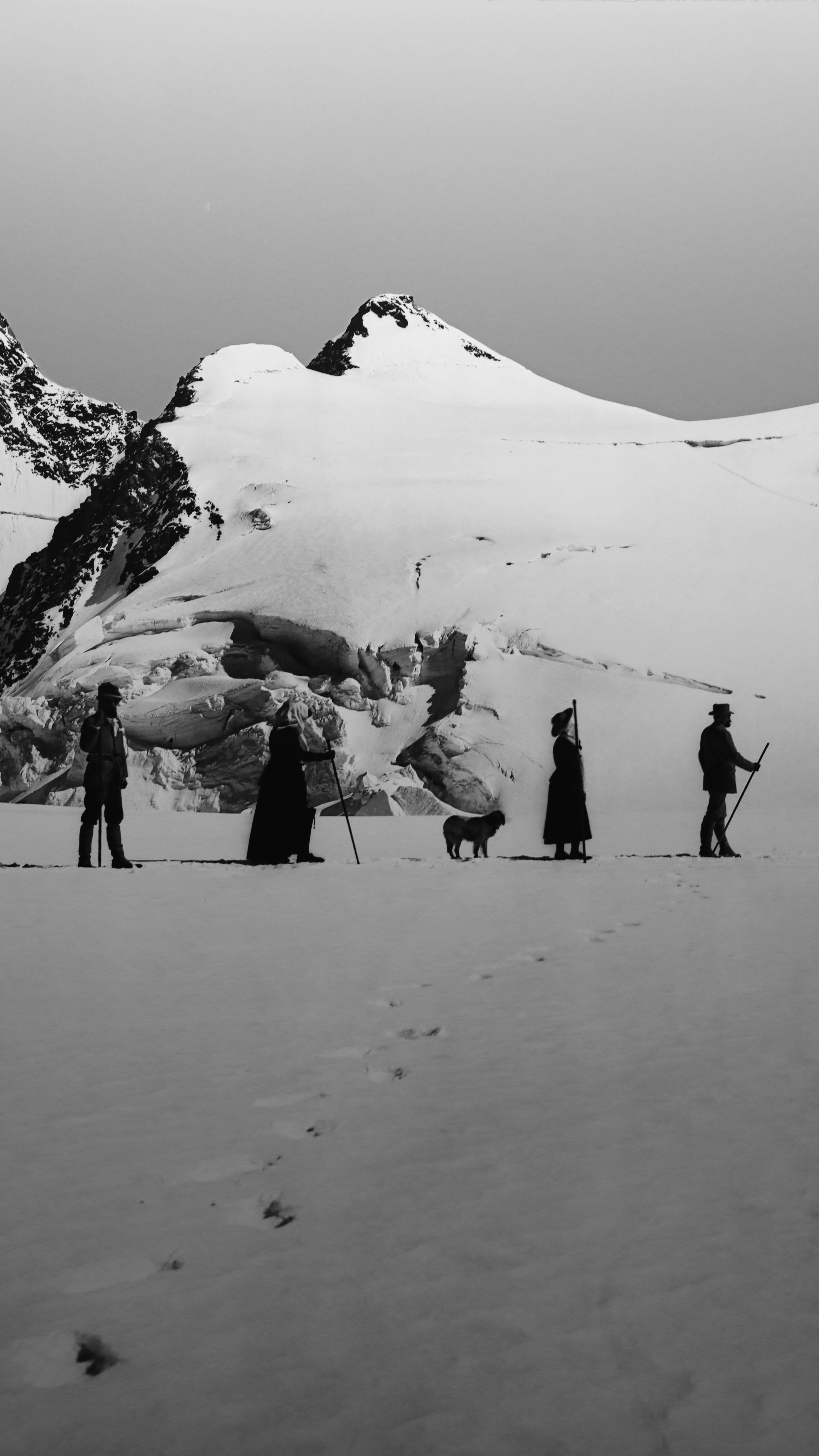 Group of explorers walking in snow-covered mountains, dramatic black and white landscape.